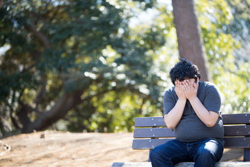 公園のベンチで悩みを抱えて泣く男性、メンタルヘルス
