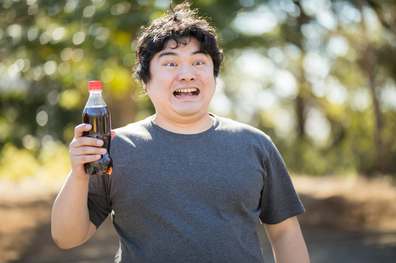 コーラボトルを手に持ち笑顔を見せる太った男性［モデル：段田隼人］