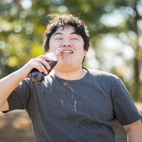 話を聞くか飲むかどちらかにしてください、とマイクを持ちながらコーラをがぶ飲みする男性の写真