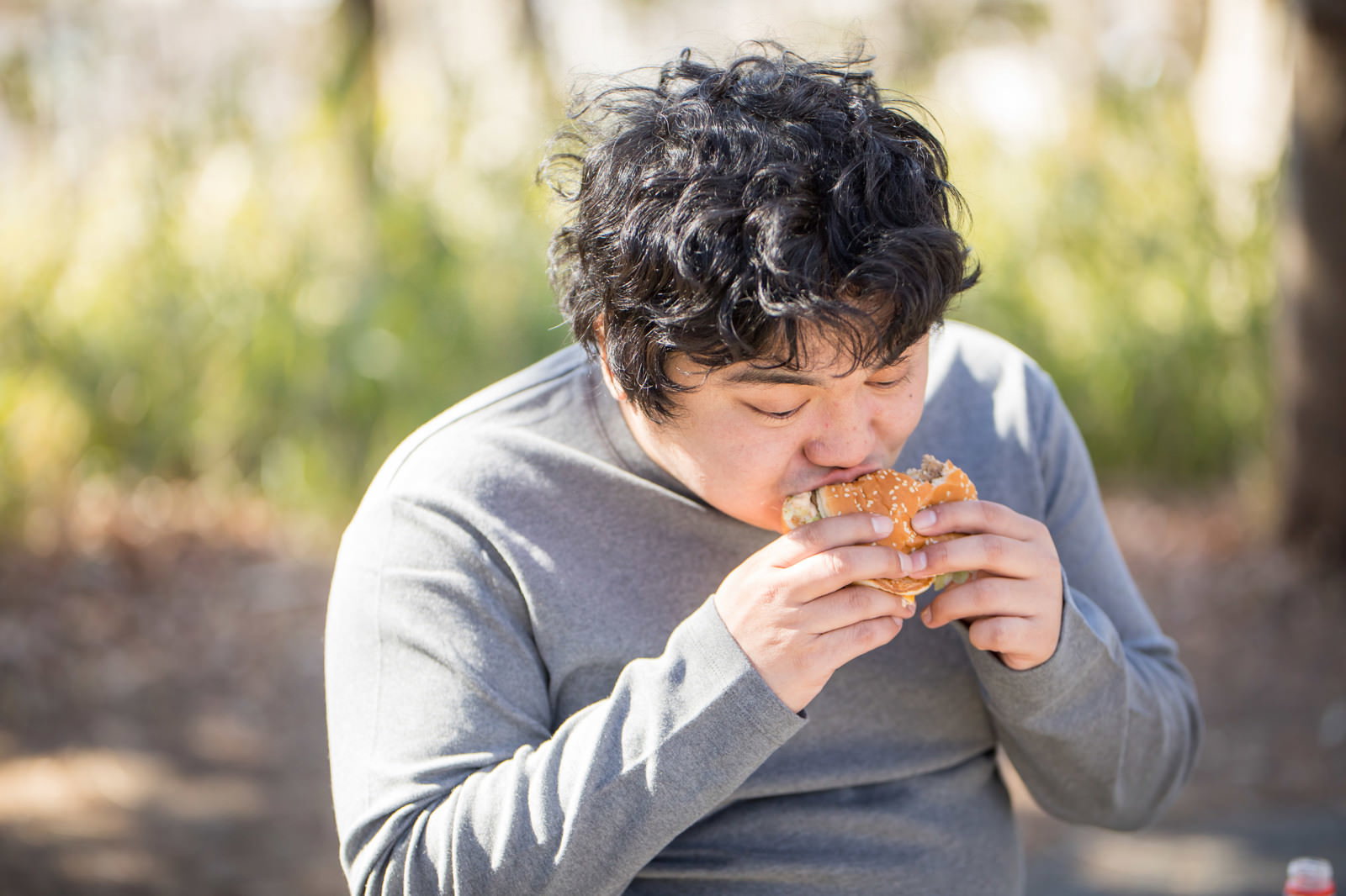 ハンバーガーを両手で持ってかぶりつく男性［モデル：段田隼人］