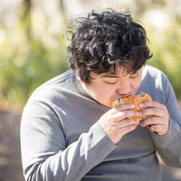 ハンバーガーを両手でかぶりつく男性の昼食シーンの写真