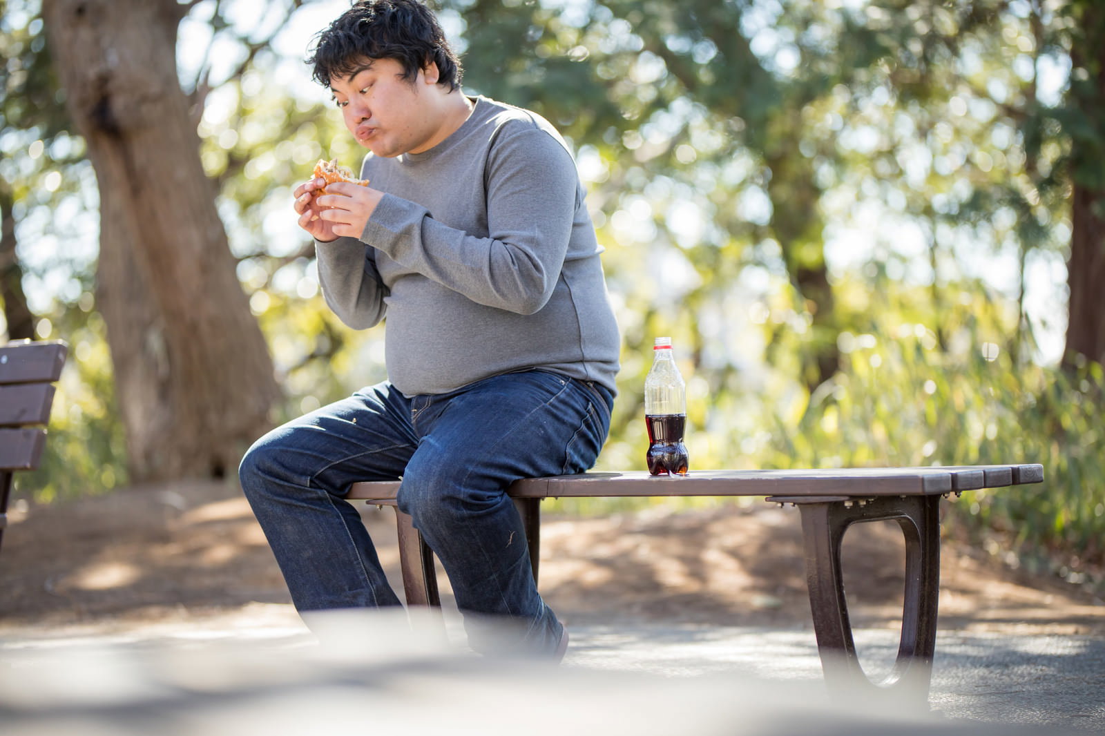 公園のベンチでハンバーガーを食べる男性［モデル：段田隼人］