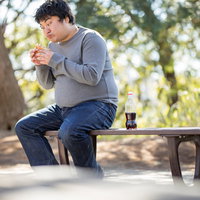 公園のベンチでハンバーガーを食べる男性の昼食風景の写真