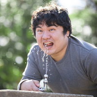 夏の公園の水飲み場で水を飲む男性の写真