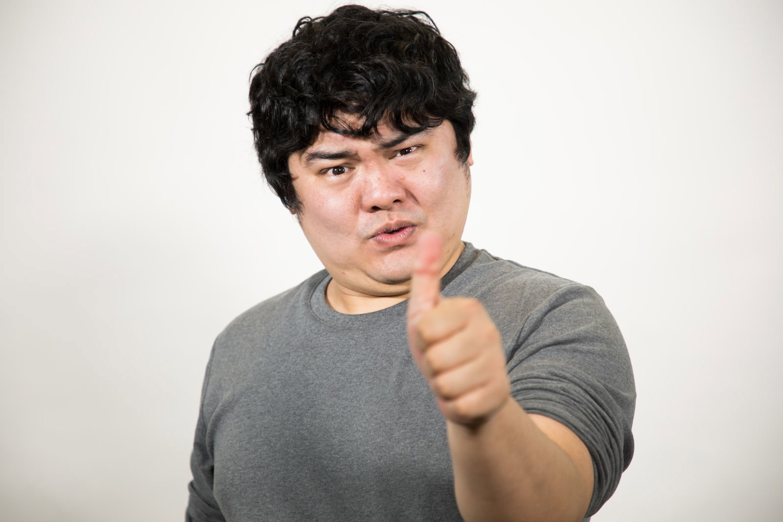 グレーシャツの男性がサムズアップするポーズ［モデル：段田隼人］