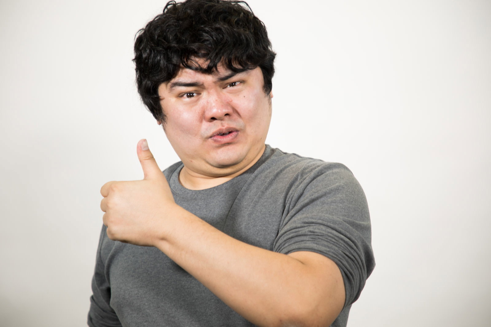 渋々サムズアップする男性［モデル：段田隼人］