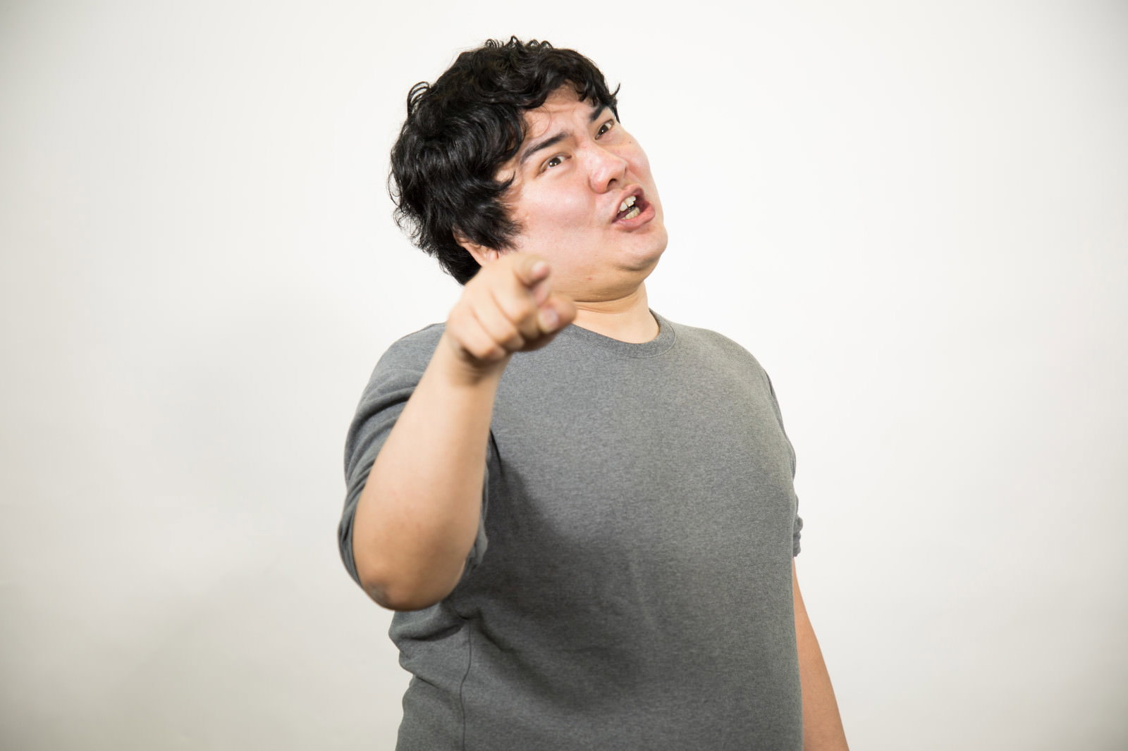 グレーのTシャツを着た男性が指を差してあざ笑う表情をしている［モデル：段田隼人］