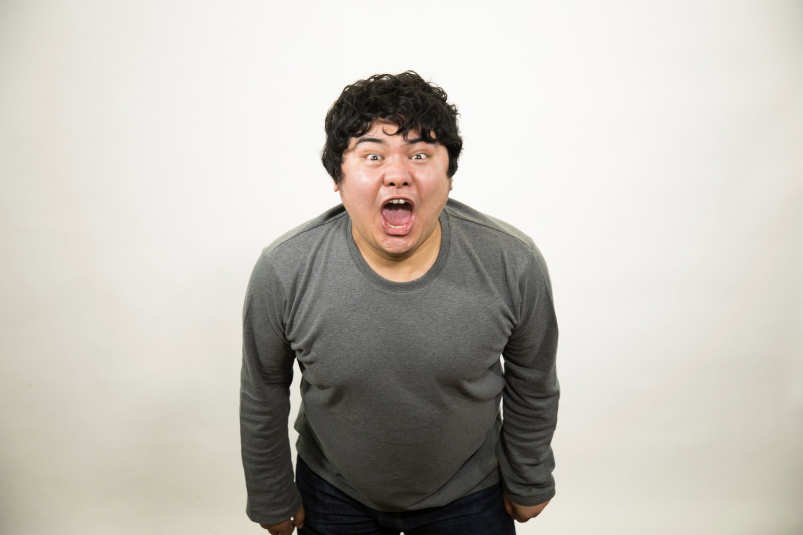口を大きく開けて叫んでいるグレーのTシャツを着た男性［モデル：段田隼人］
