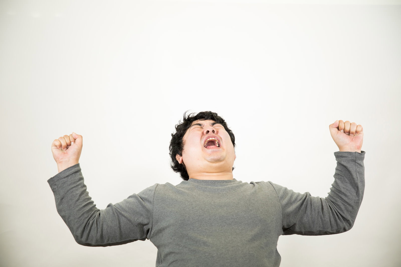 グレーのトップスを着た男性が両手を上げて歓喜している［モデル：段田隼人］