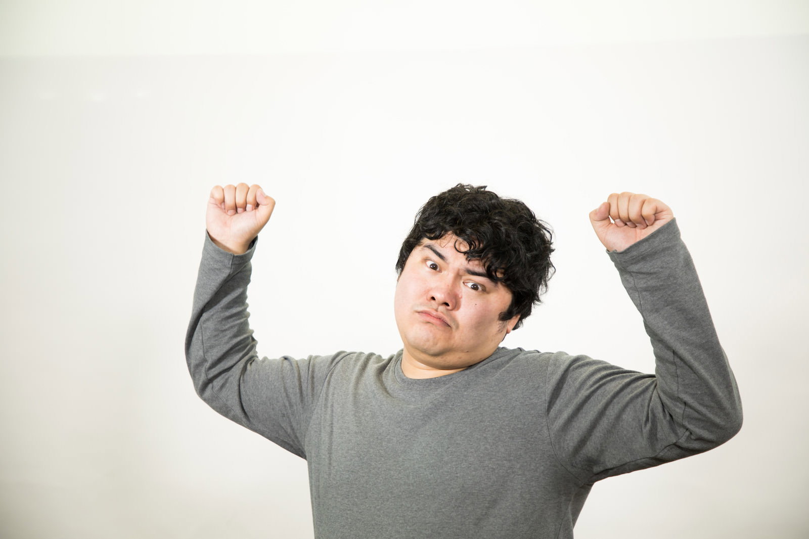 グレーのトレーナーを着た男性が両手を上げて勝利のポーズをとっている［モデル：段田隼人］