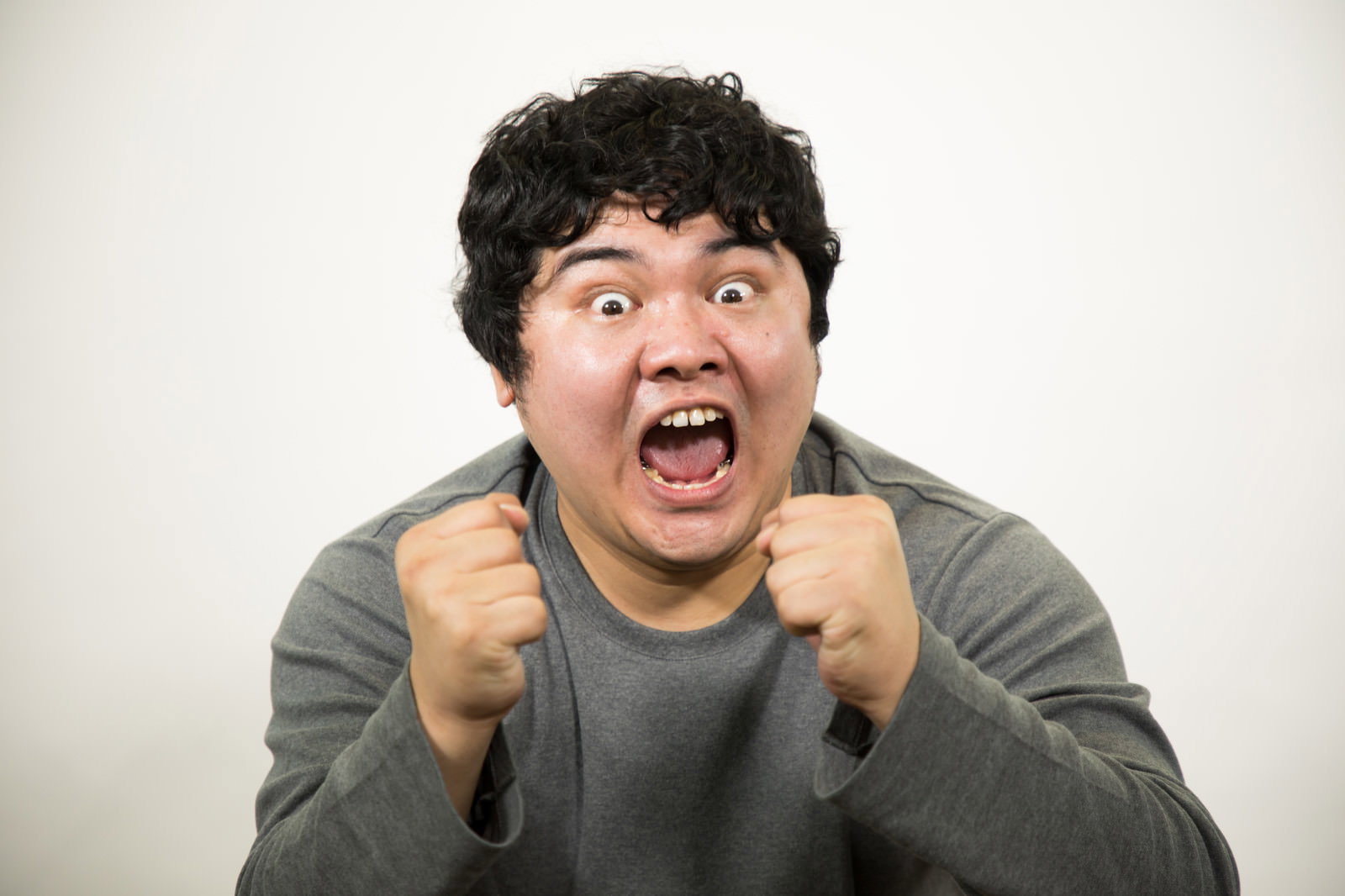 グレーの服を着た男性が両手で拳を作り大きく口を開けて叫んでいる［モデル：段田隼人］