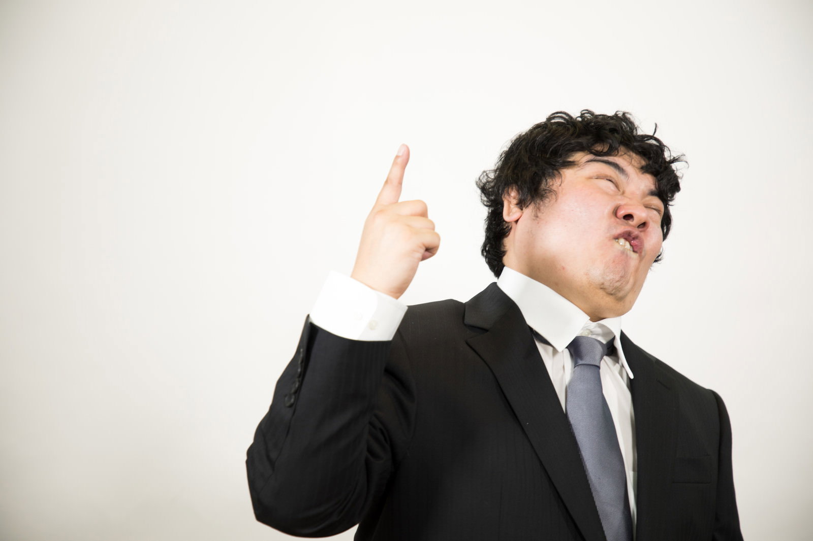 スーツの男性が指を立てて上空を指差し張り切っている［モデル：段田隼人］
