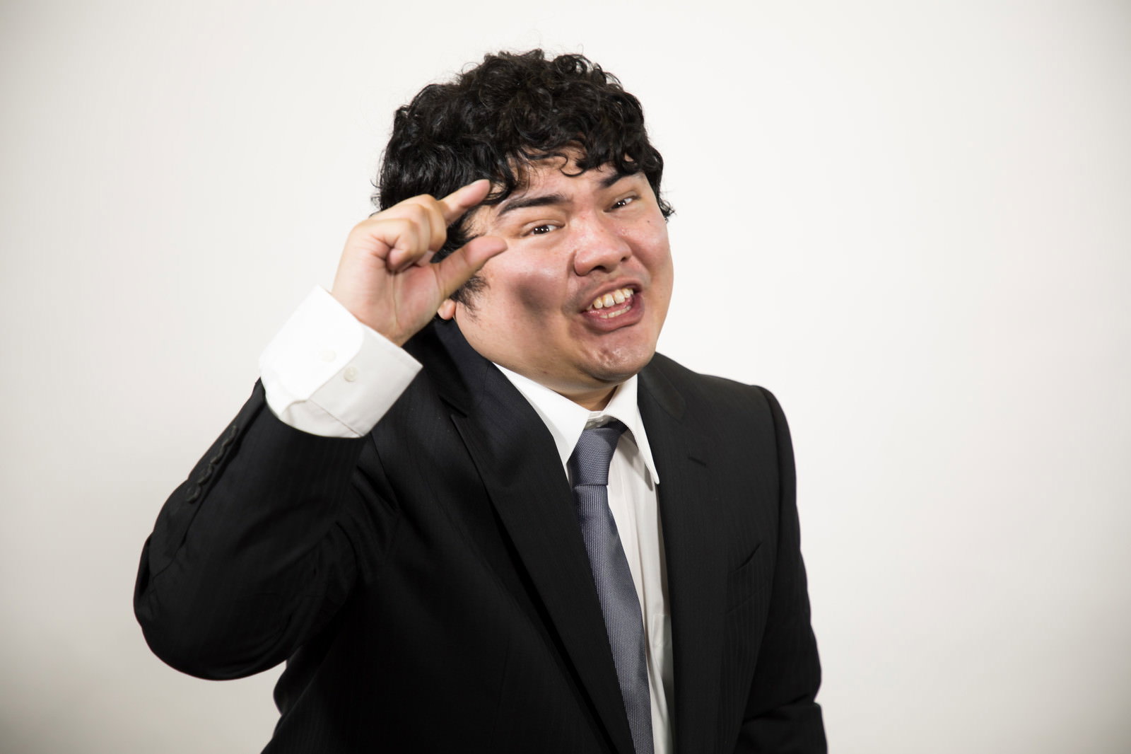 額に手を当てて苦笑いを浮かべているスーツ姿の男性［モデル：段田隼人］