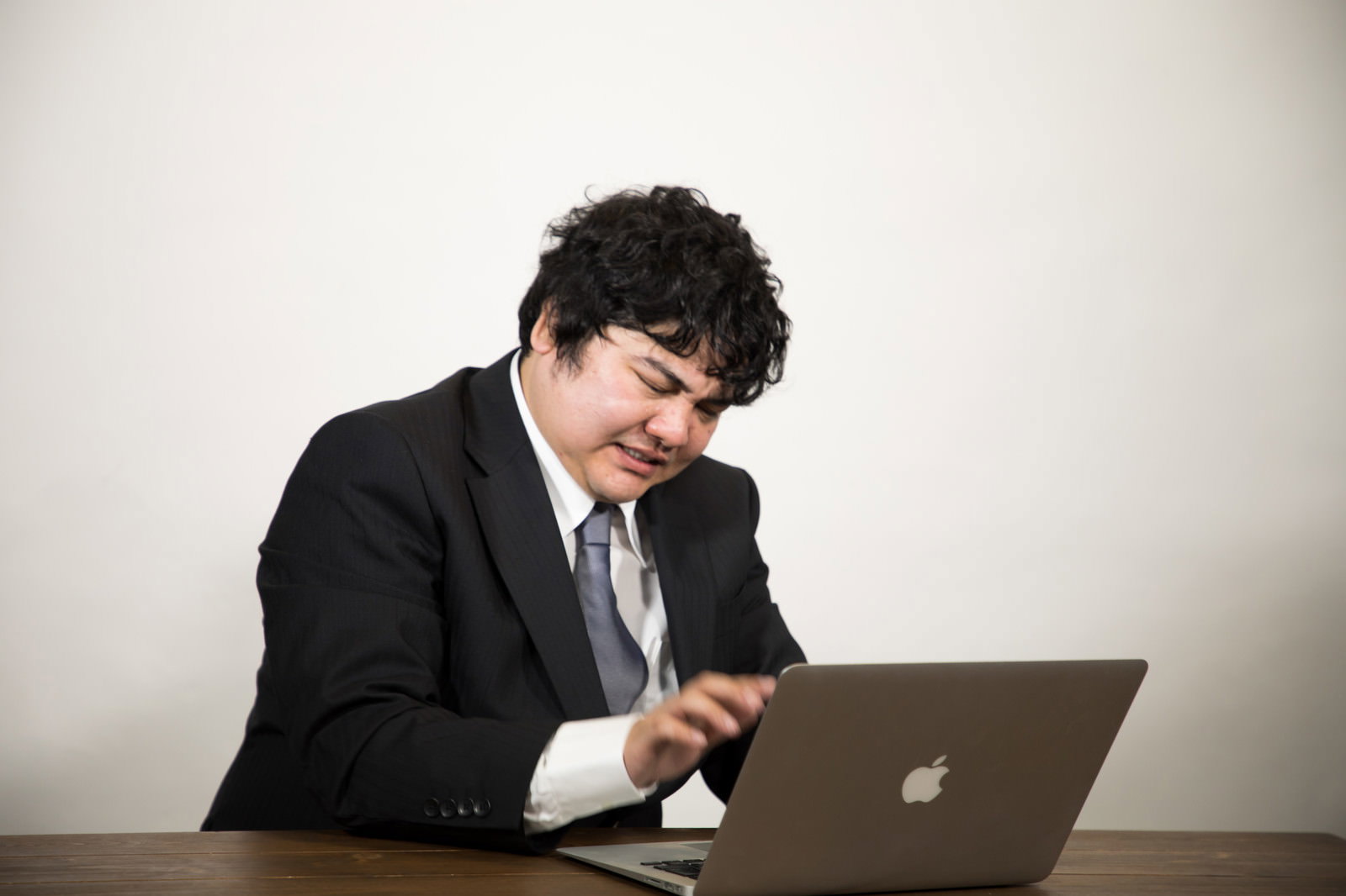 ノートパソコンの前で頭を抱えて悩んでいるスーツ姿の会社員男性［モデル：段田隼人］
