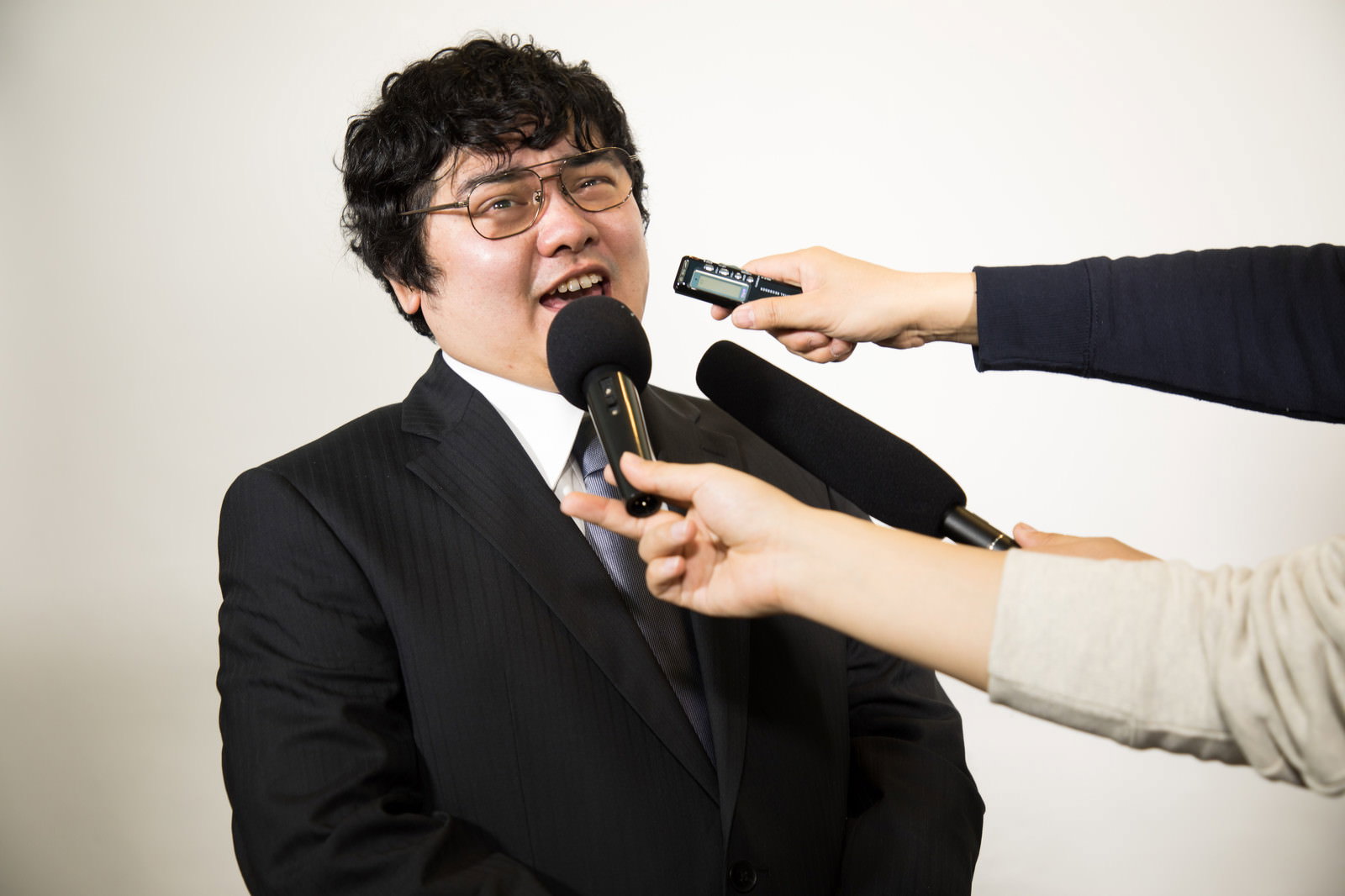 複数のマイクを向けられ質問に答える男性役員［モデル：段田隼人］