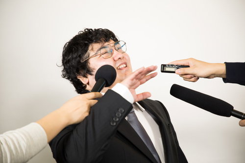 複数のマイクを向けられ執拗な囲み取材を受ける男性