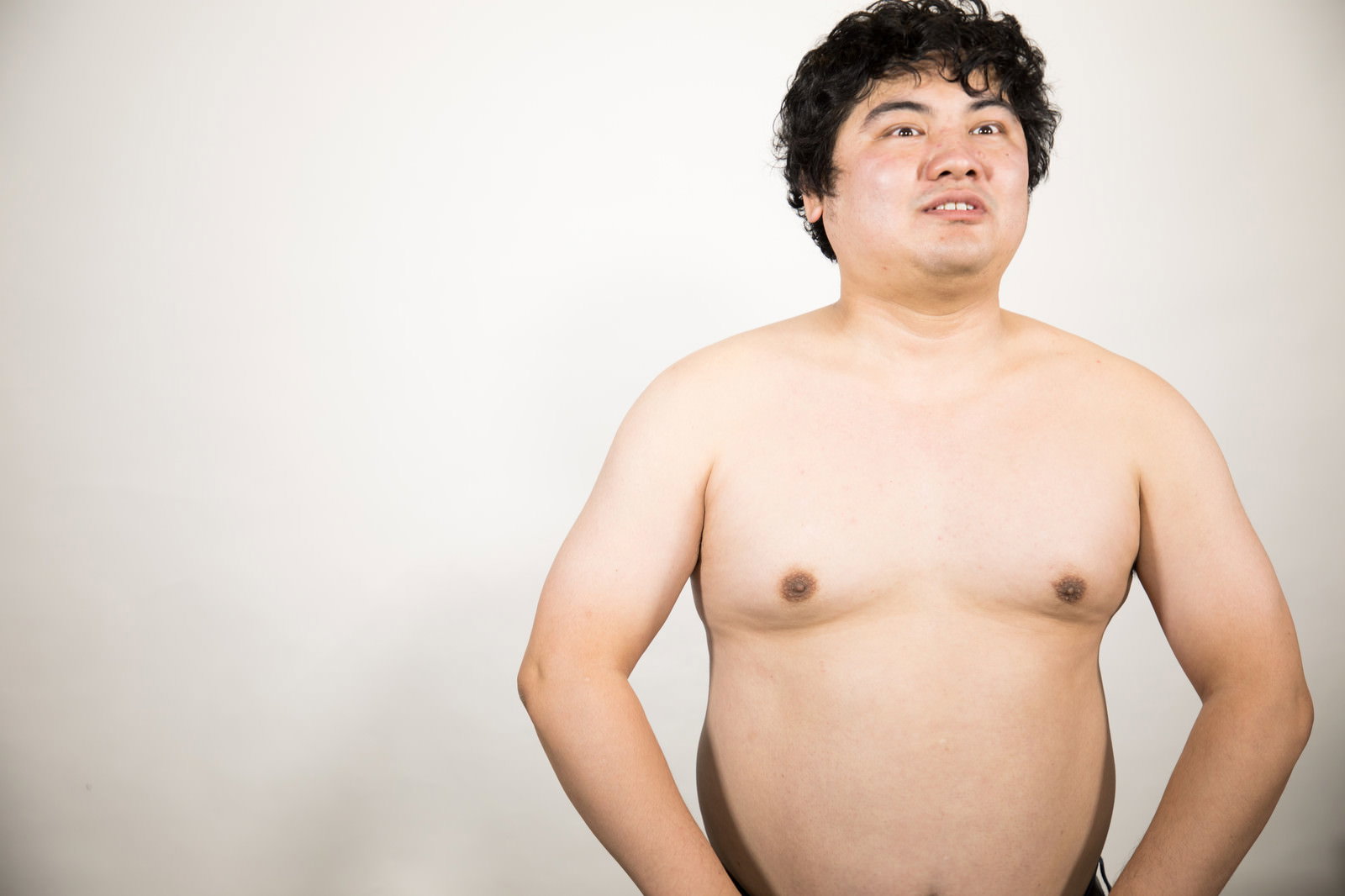 腰に手を当てて立つ上半身裸の男性［モデル：段田隼人］