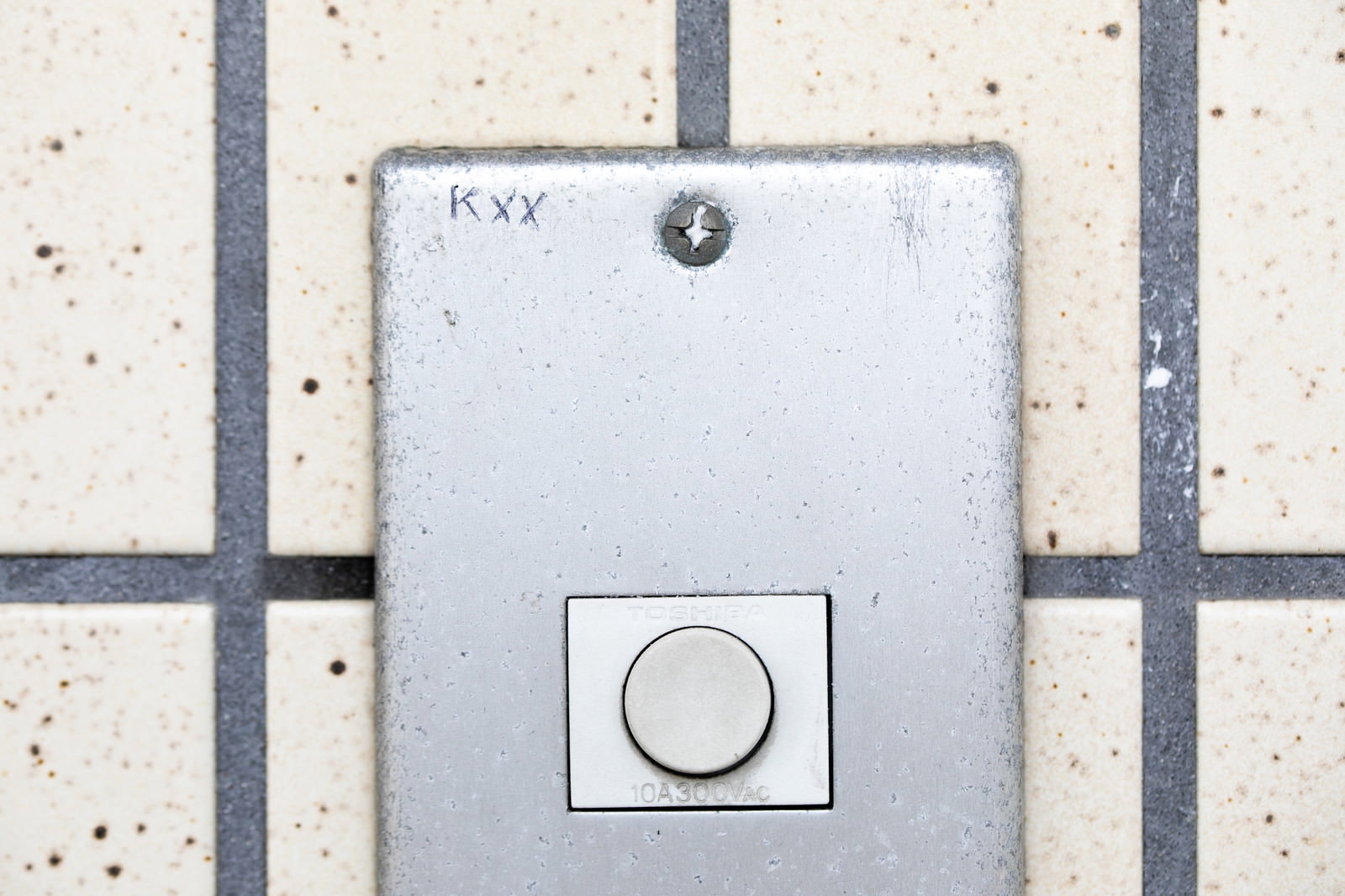 玄関タイル壁に設置されたインターホン、表面にKxxのマーキングと下部に円形の押ボタンが見える