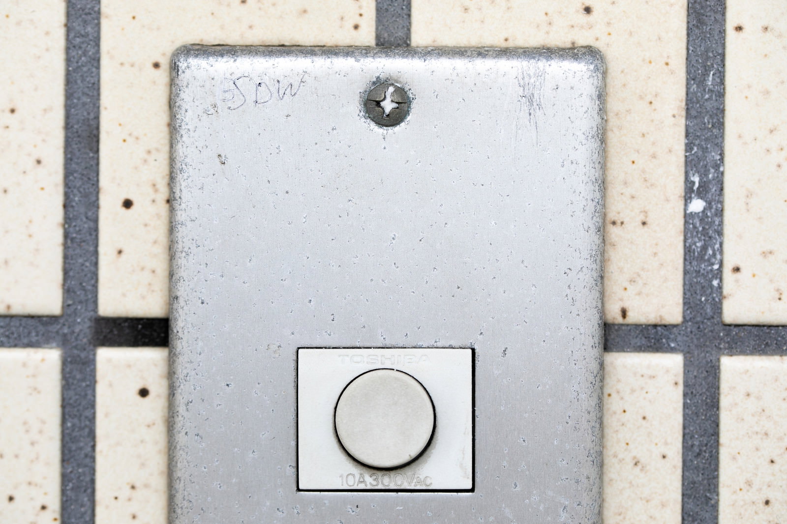 白いタイル壁に付けられたメタリック色のインターホン。上部にSWDと刻印されたマーキングが見える