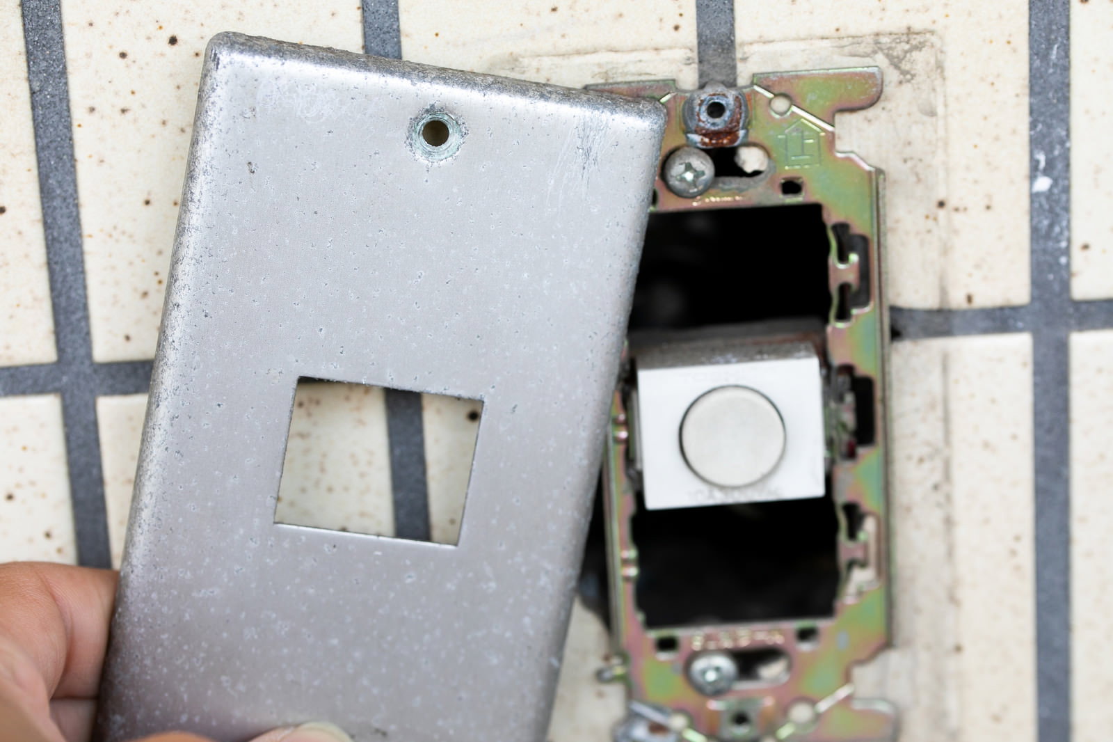 白い壁からアナログの玄関チャイムを取り外している手元の様子