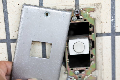 白い壁に設置されたアナログの玄関チャイムを取り外す