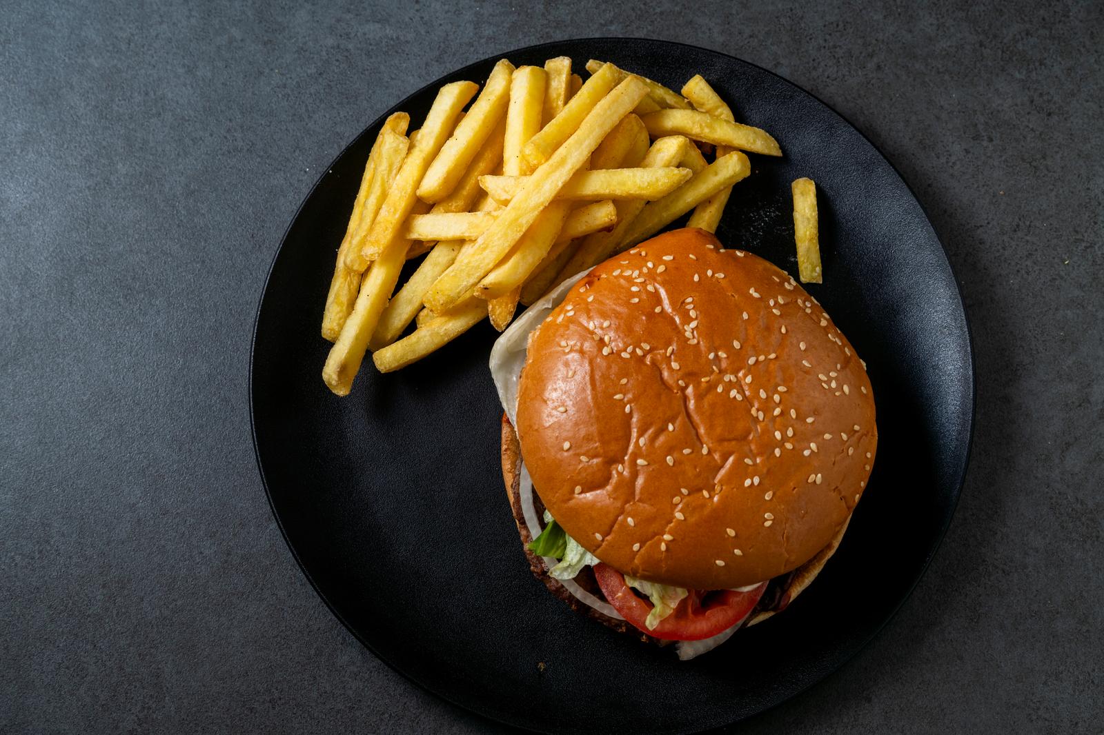 Sesame bun hamburger and fries on a black plate