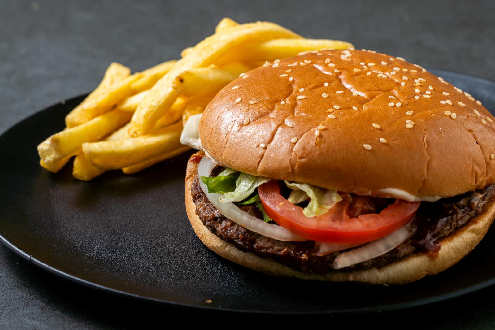 Sesame bun burger and golden French fries on a black plate