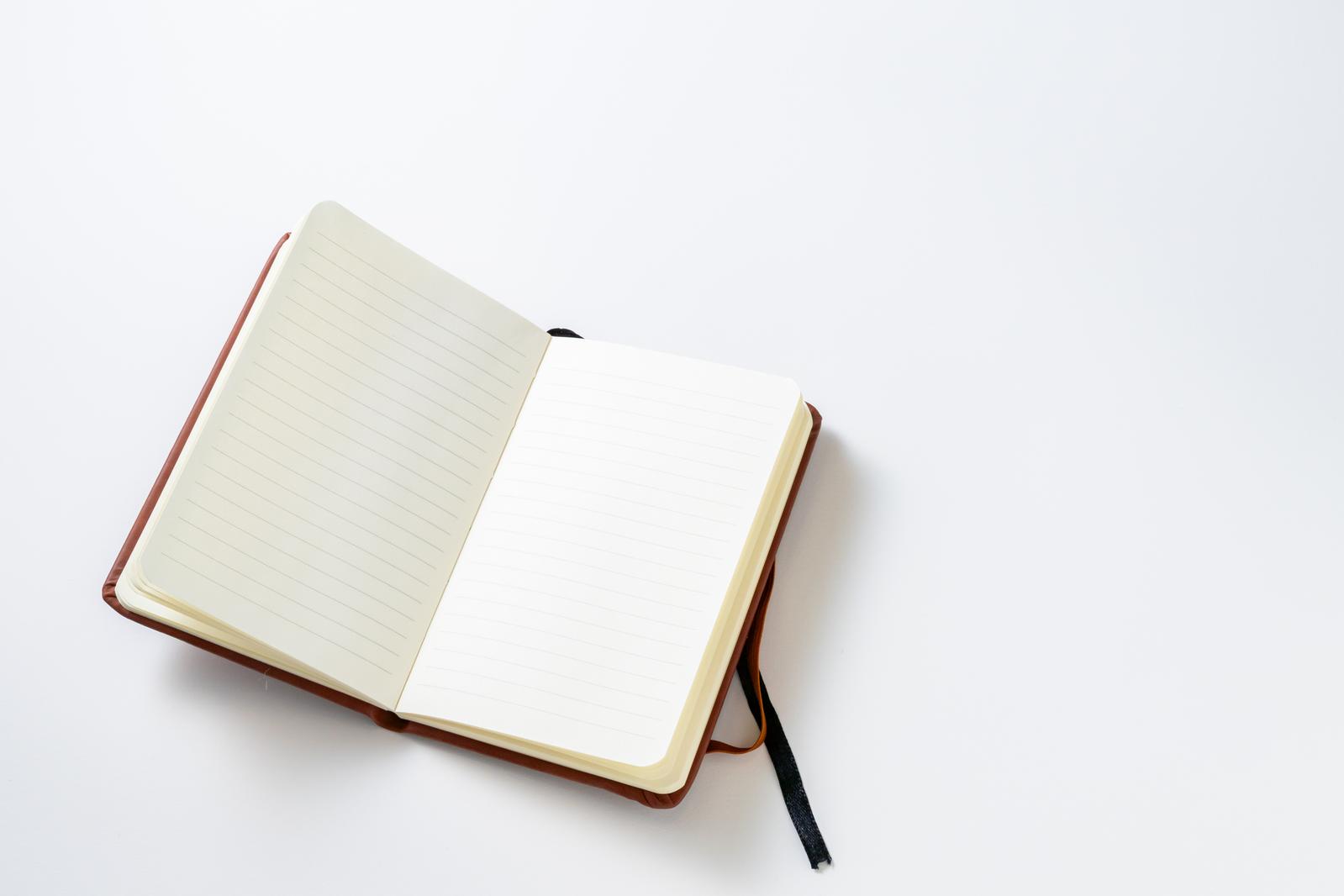 Open brown notebook with a black pen on a white background, with lined pages