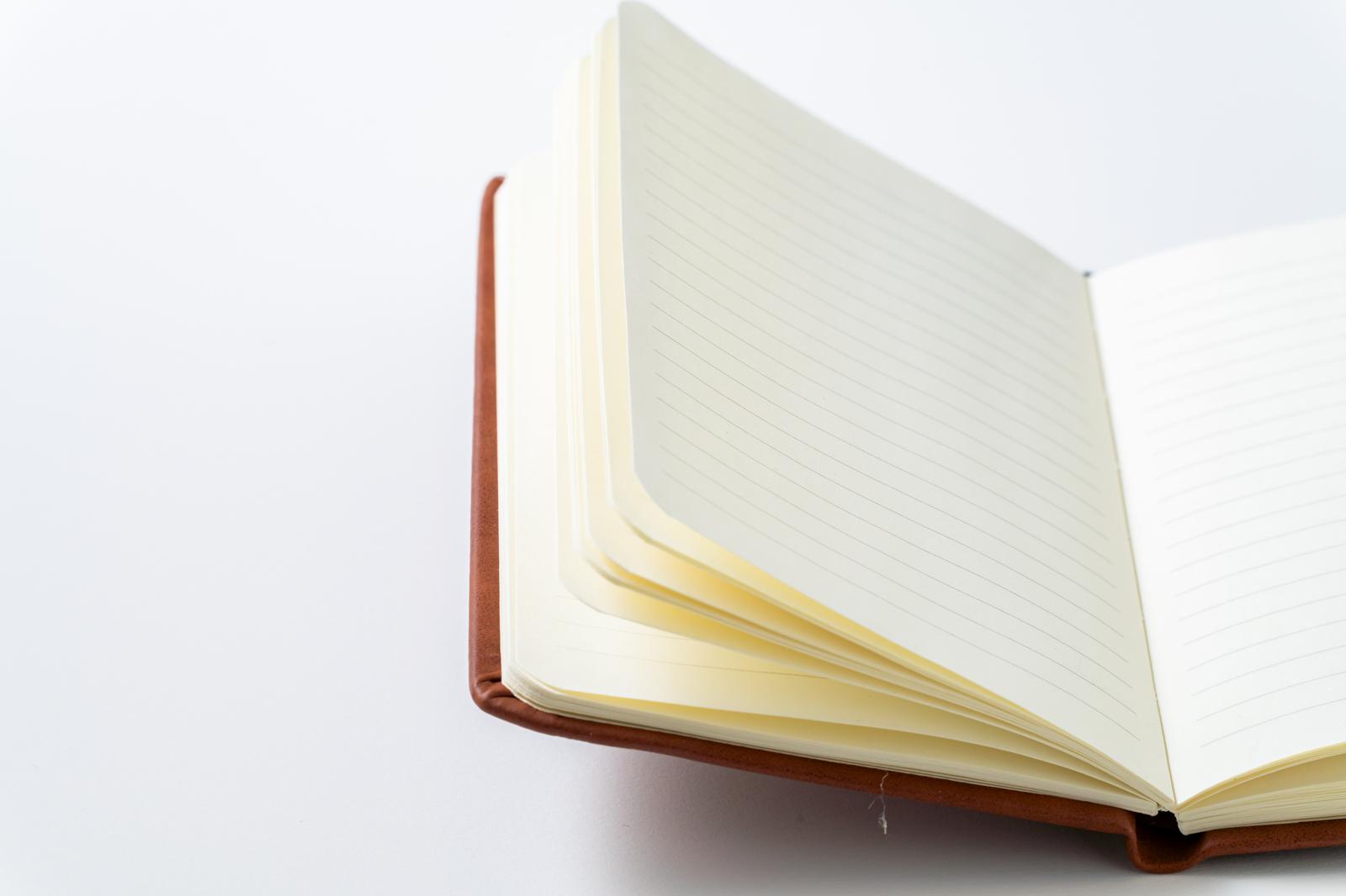 A brown notebook with open pages showing ruled lines against a white background