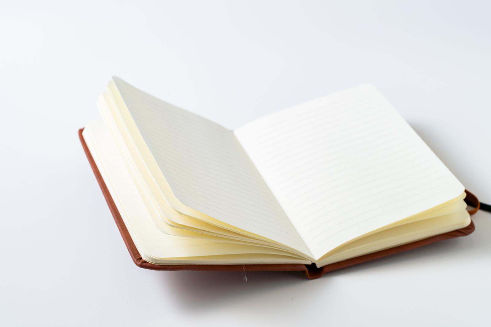 A notebook with a brown leather-like cover is open, revealing blank white pages.