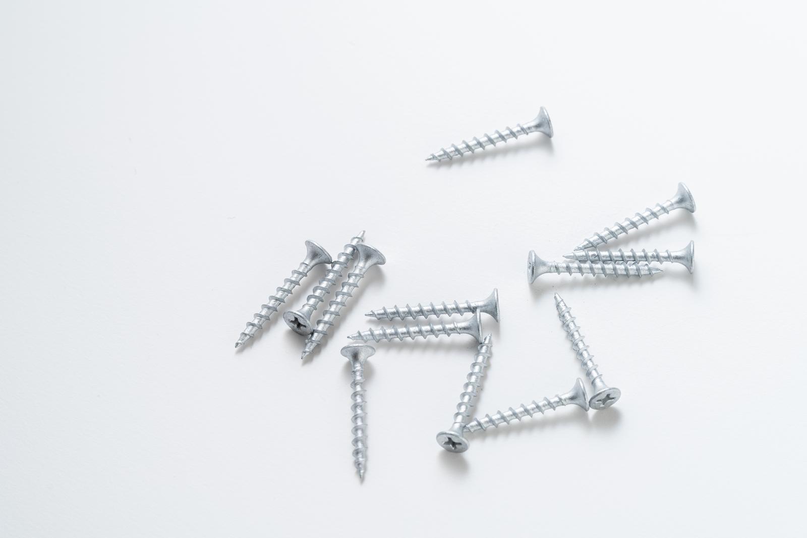 Multiple silver-colored screws and nails scattered on a white background