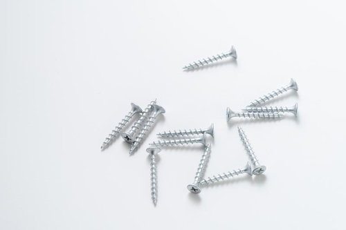 白い背景に無造作に散らばって置かれたシルバー色のビスと釘