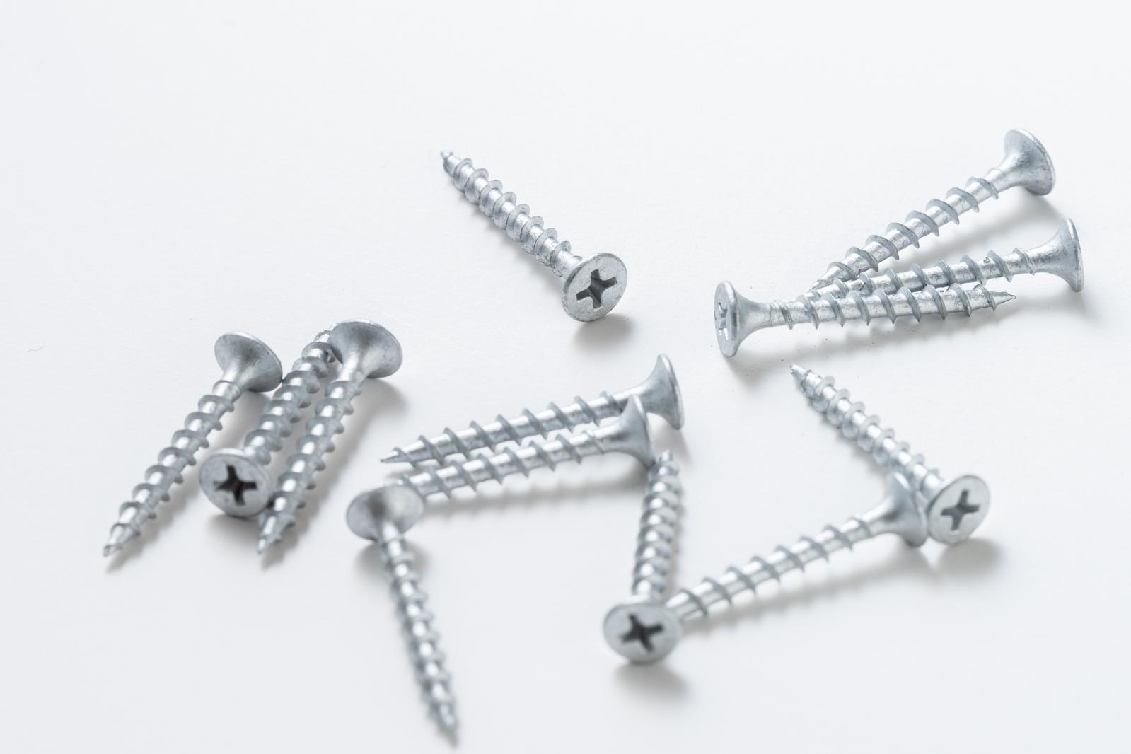Scattered silver screws and bolts of different sizes on a white background