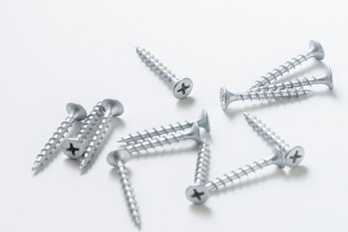 白い背景に無造作に配置された銀色のネジとビスの工具類