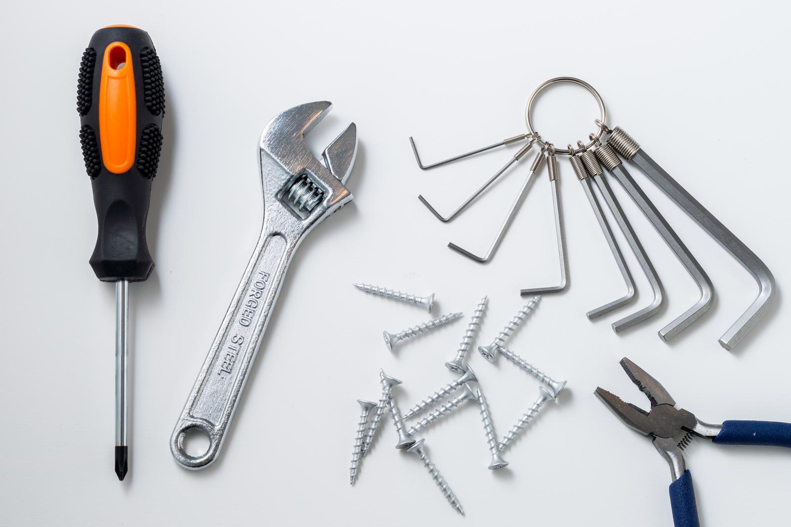 A set of tools including drivers, monkey wrenches, hex keys, pliers, and screws, arranged on a white background.