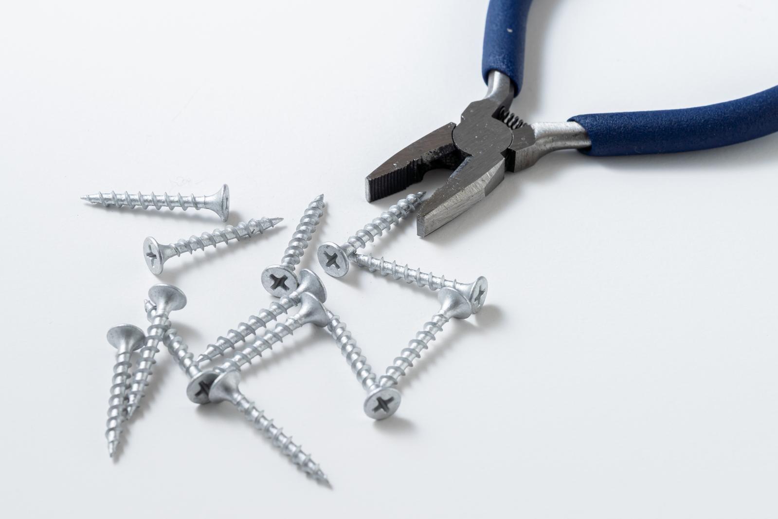 Blue handle pliers and silver screws scattered on a white background