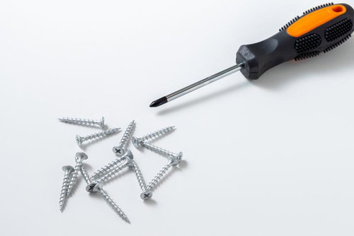 白背景に置かれたオレンジ色のプラスドライバーと散らばったネジ