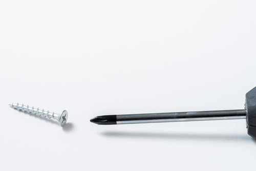 白い背景に置かれたプラスドライバーとネジ