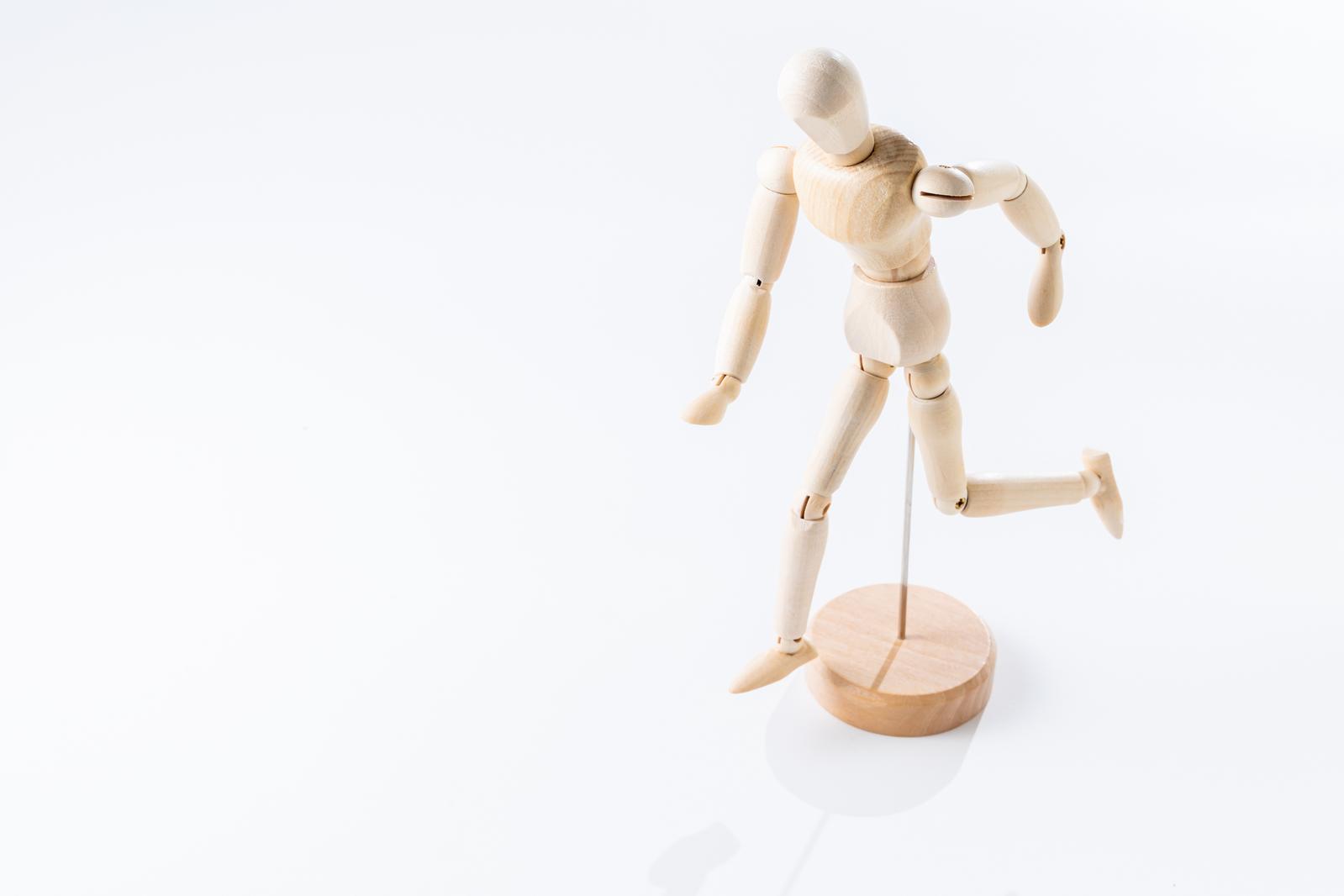 Wooden mannequin figurine in running pose with circular pedestal on white background