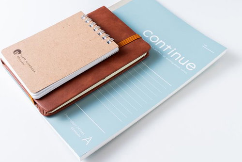 デスクに並べられたリングノートと革製手帳とブルーのファイル