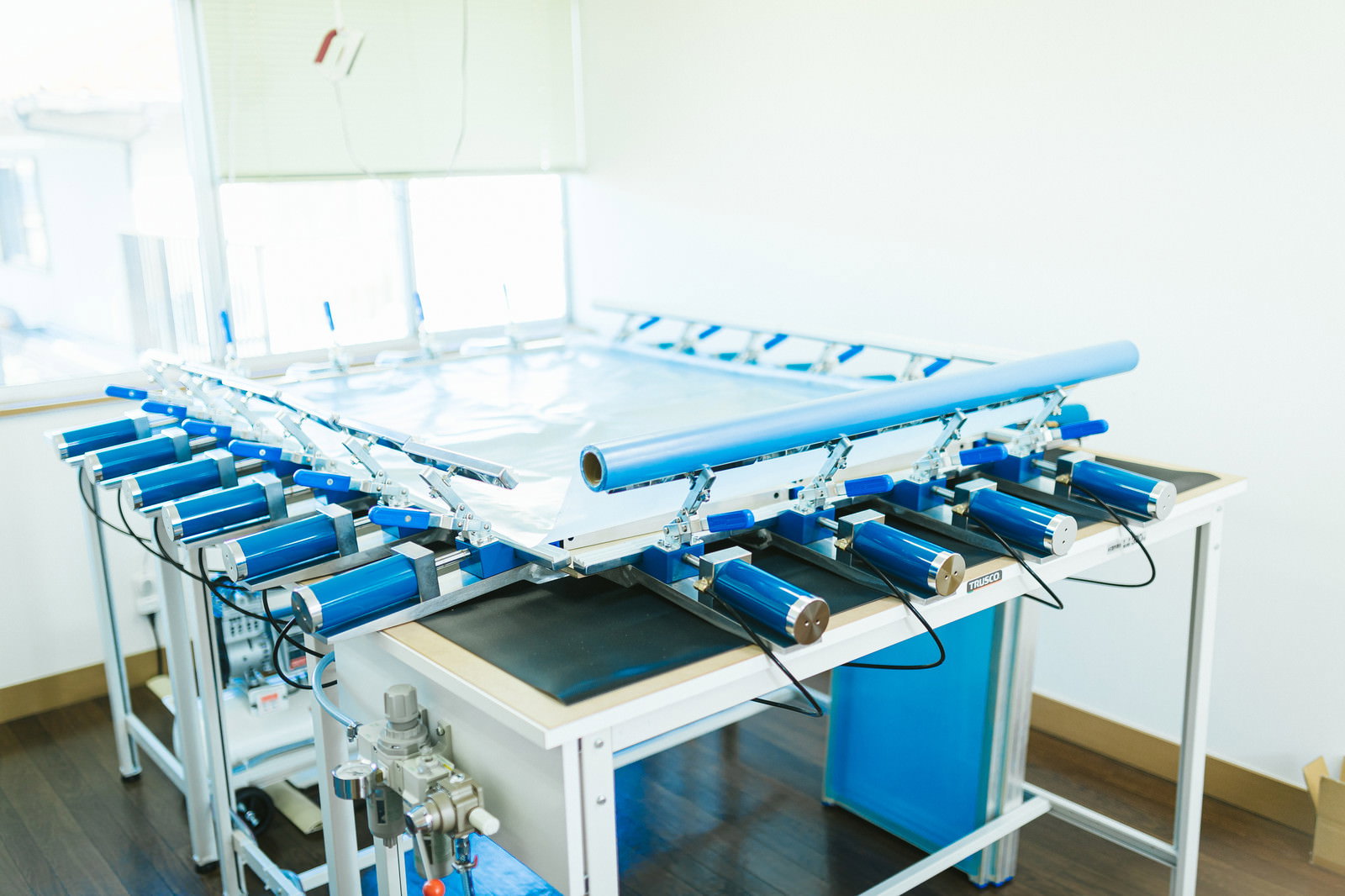 青いフレームが並ぶシルクスクリーンの紗張り作業台