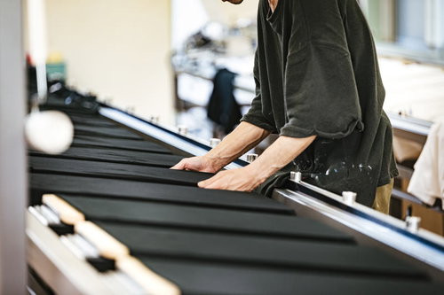 長台に置かれた黒いTシャツのシワを伸ばすシルク印刷の職人