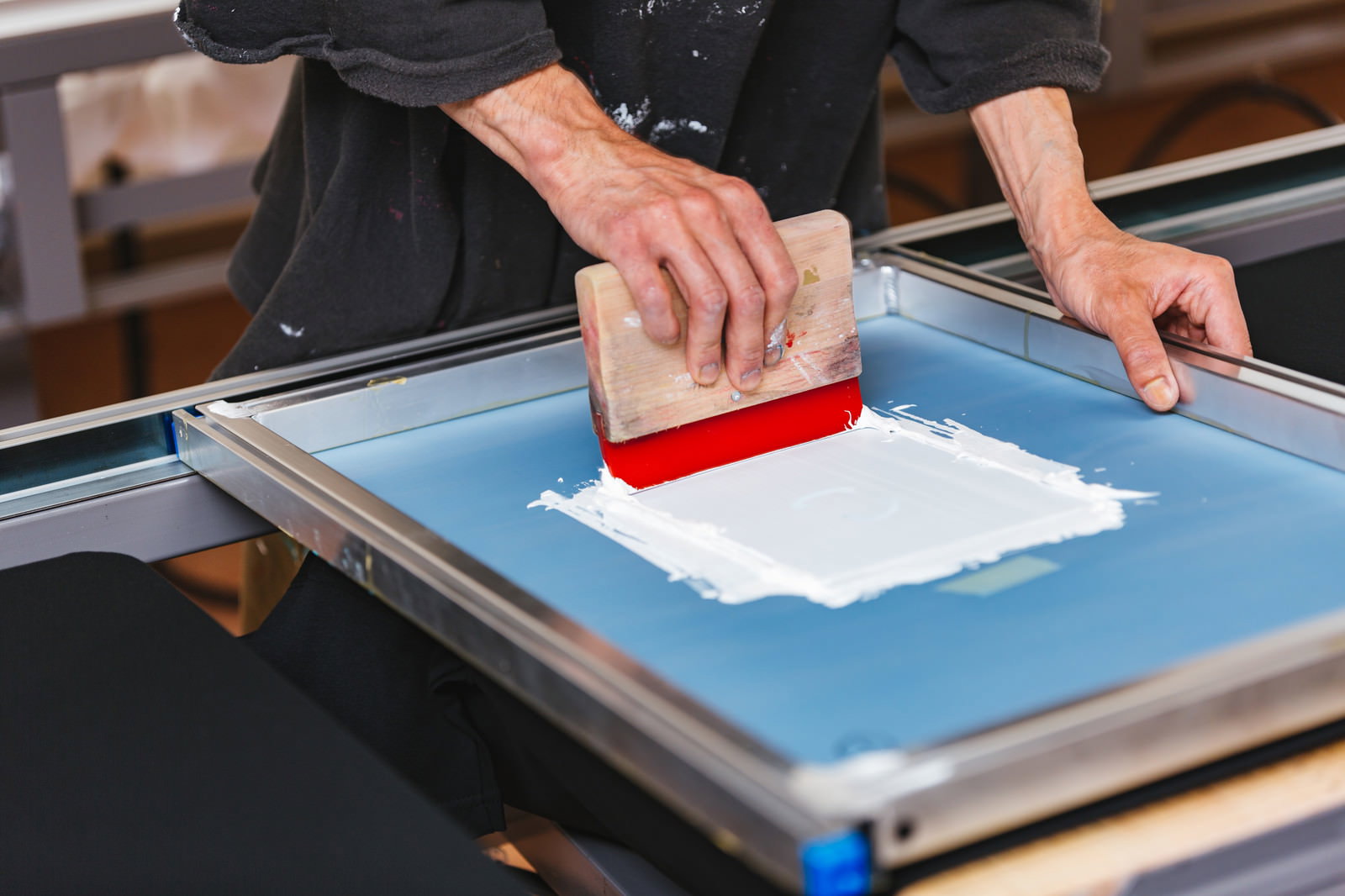 スキージを使って青い印刷台の上で白いインキを刷る手元