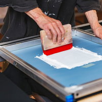 スキージを使って白いインキを手刷りするシルク印刷の工程の写真