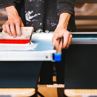 赤いインキで一枚一枚手刷りするTシャツのシルクスクリーン印刷の写真