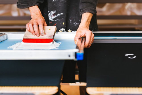 赤いインキで一枚一枚手刷りするTシャツのシルクスクリーン印刷