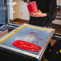 水性インキ（赤）を版に乗せるシルク印刷の職人作業の写真