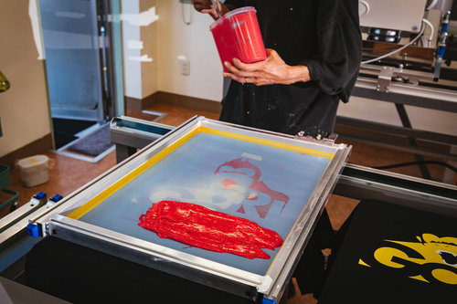 水性インキ（赤）を版に乗せるシルク印刷の職人作業