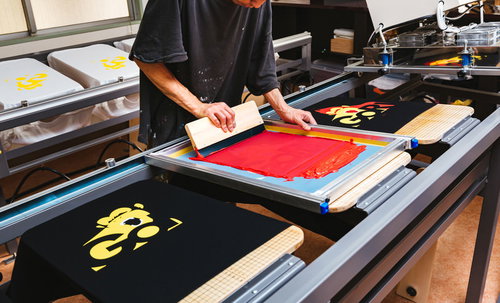 シルク印刷でTシャツに黒いインキを着色する職人の作業