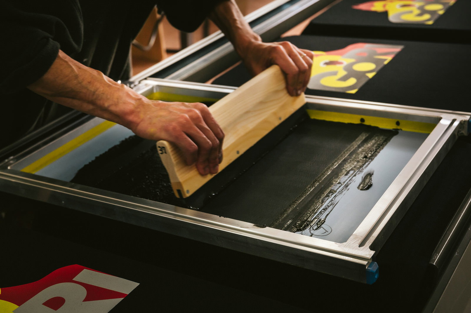 スキージーで黒Tシャツに黒インキを塗り広げる職人の手元